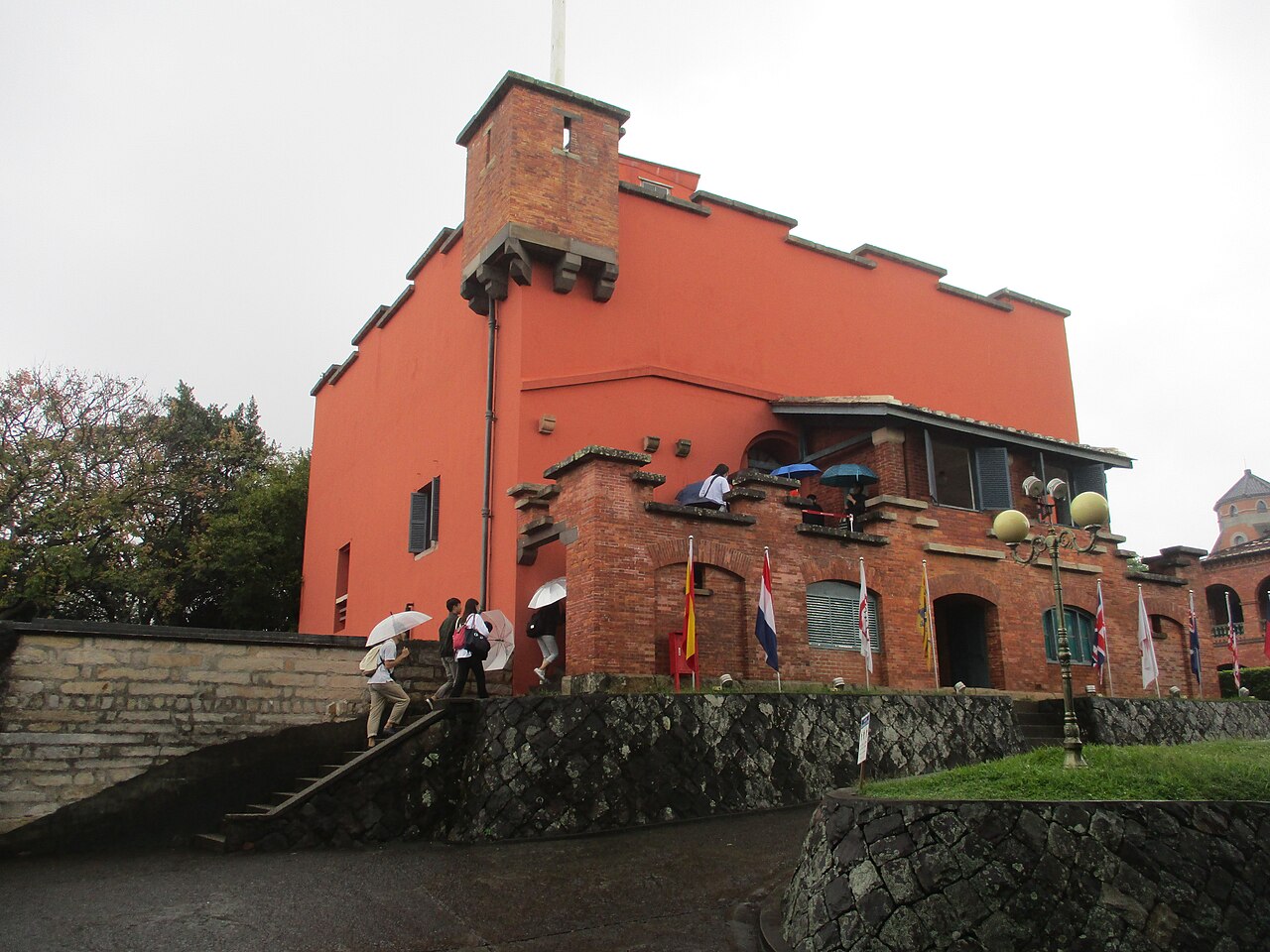 Fuerte de Santo Domingo de Tamsui, edificio de muros rojos con almenas, con las banderas de las administraciones que lo ocuparon